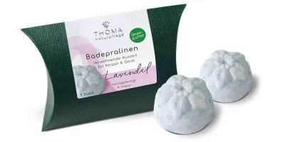 Zwei hellblaue Badepralinen vor dunkelgrüner Verpackung mit weißer Aufschrift Badepralinen Lavendel, handgefertigt und vegan von der Naturseifen Manufaktur Uckermark.