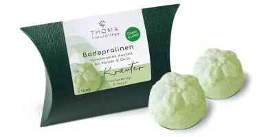 Zwei grüne Badepralinen vor dunkelgrüner Verpackung mit weißer Aufschrift Badepralinen Kraeuter, handgefertigt und vegan von der Naturseifen Manufaktur Uckermark.