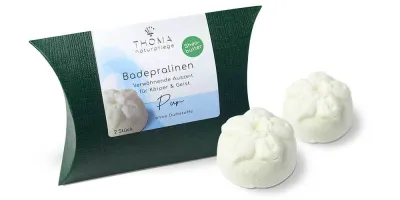Zwei weiße Badepralinen vor dunkelgrüner Verpackung mit weißer Aufschrift Badepralinen Pur, ohne Duftstoffe, handgefertigt und vegan mit Sheabutter von der Naturseifen Manufaktur Uckermark.