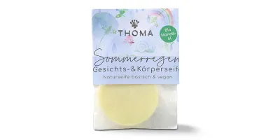 Runde, gelbliche Mini Seife in transparenter Verpackung mit blauer Aufschrift Sommerregen, Mandelölseife mit Kokosmilch vegan von der Naturseifen Manufaktur Uckermark.