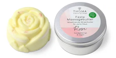 Gelbe feste Massagebutter in Rosenform neben silberner Dose mit weiß-rosafarbener Aufschrift Feste Massagebutter Rose, verwöhnende Körperbutter mit Wildrosenoel, handgefertigt und vegan von der Naturseifen Manufaktur Uckermark.